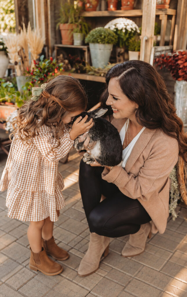 Woman and young girl gently cuddle a black-and-white rabbit on a small vintage rug in the Grange Garden courtyard.